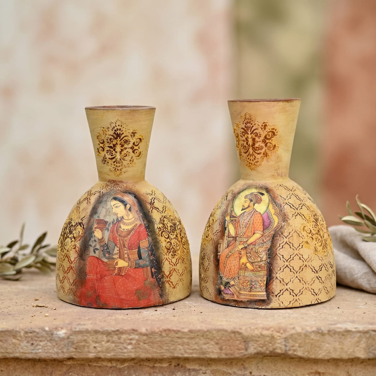 Two decorative ceramic vases with a warm beige and gold tone, featuring traditional painted figures and ornate patterns, displayed on a stone surface.
