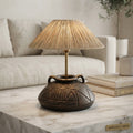 A decorative table lamp with a textured beige fringed shade and an antique bronze carved ceramic base, styled on a marble table in a living room setting.