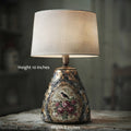A vintage-style table lamp with a textured beige fabric drum shade and an ornate distressed ceramic base featuring a floral and bird motif. White text overlays indicate dimensions: 'Height 10 inches' on the left and 'Width 8 inches' at the bottom.